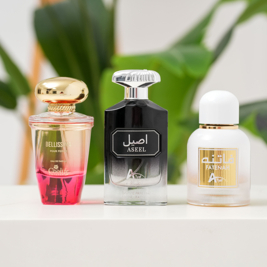 Three perfume bottles with visible branding on a white surface with a blurred green plant background.