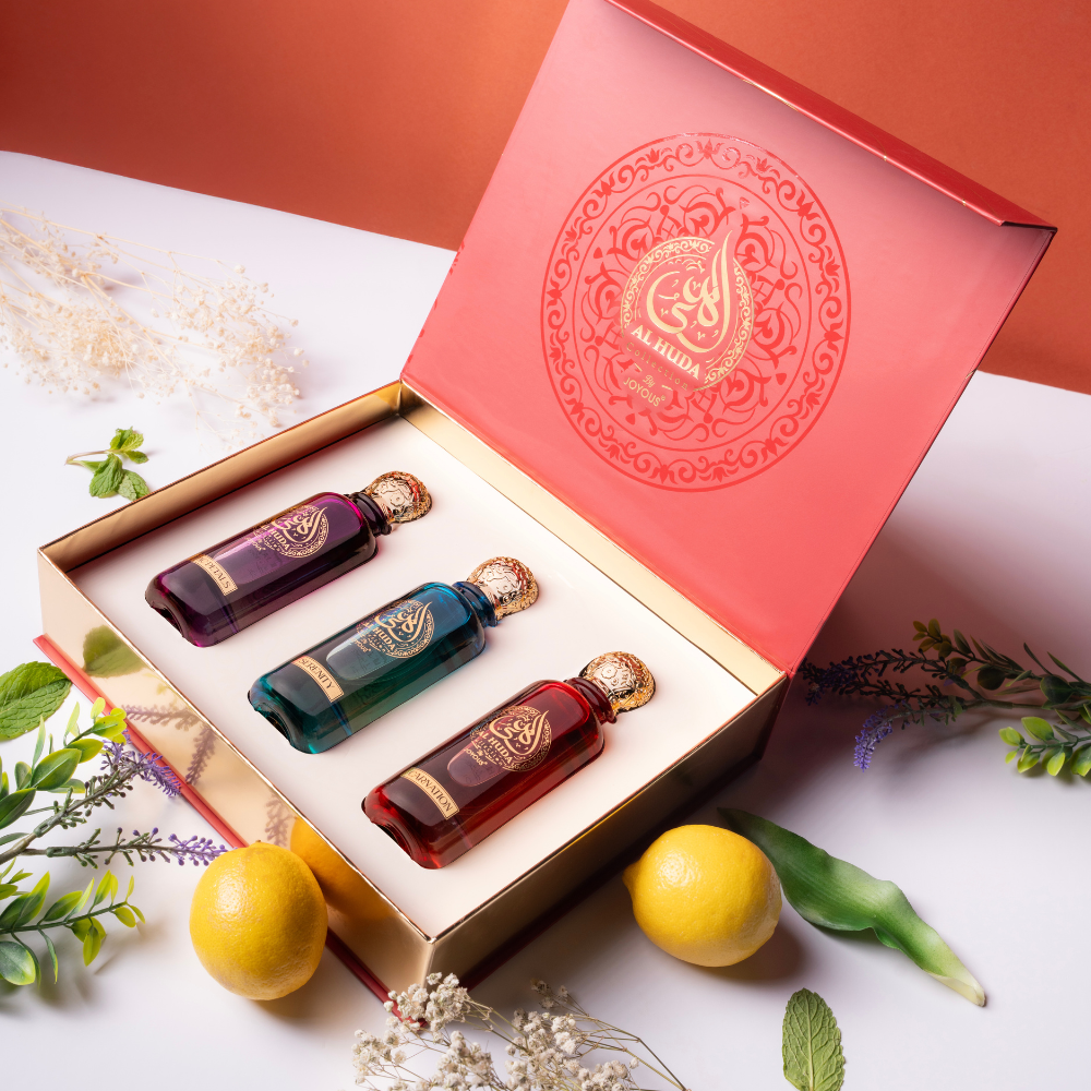 Three small bottles of perfume in a decorative box with a red lid featuring gold patterns, surrounded by lemons and greenery on a white surface.