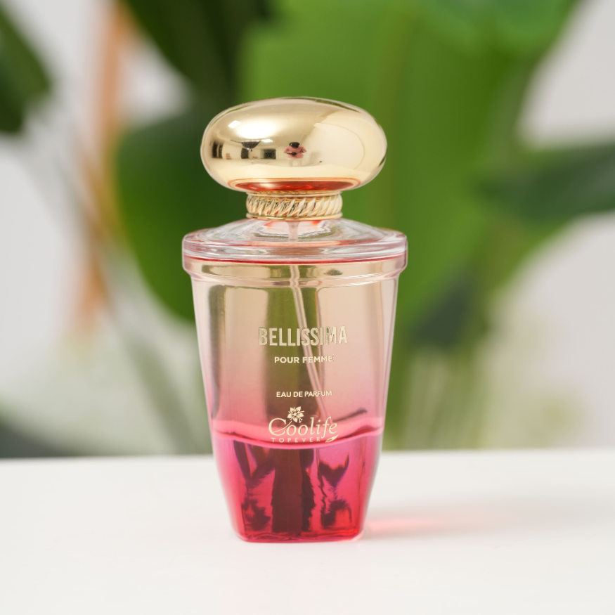 Perfume bottle with gold cap and pink gradient design on a blurred green background